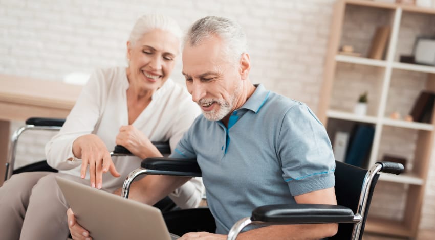 Caregiver helping a man in a wheelchair use a communication tablet at home in Fort Myers, Florida