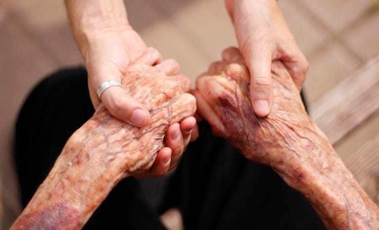 Caregiver gently holding hands with an elderly person during respite care at home in Fort Myers, Florida