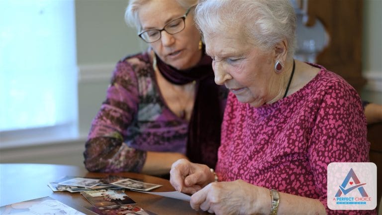 Elderly mother and her adult daughter looking through old family photographs together at a table