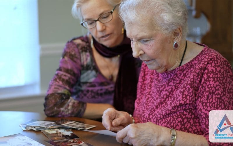 Elderly mother and her adult daughter looking through old family photographs together at a table